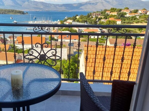Ein Balkon mit Tisch und Stuhl mit Blick auf einen Yachthafen und eine Küstenstadt mit roten Dächern.