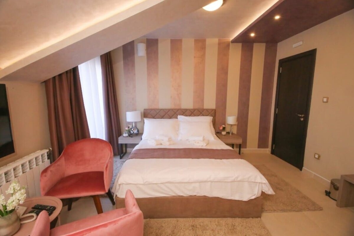 A hotel room with a bed, a red chair, a bedside table, and a television.