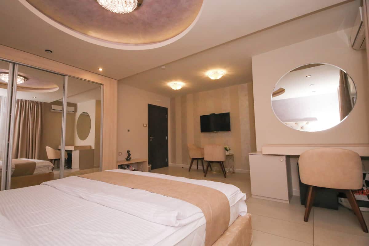 A hotel room with a large bed, a desk, a chair, a mirror, and a television.