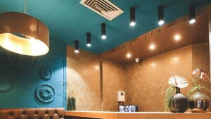 Uma área de recepção com um banco de couro estofado, uma mesa de madeira com uma xícara de café e um luminário moderno.