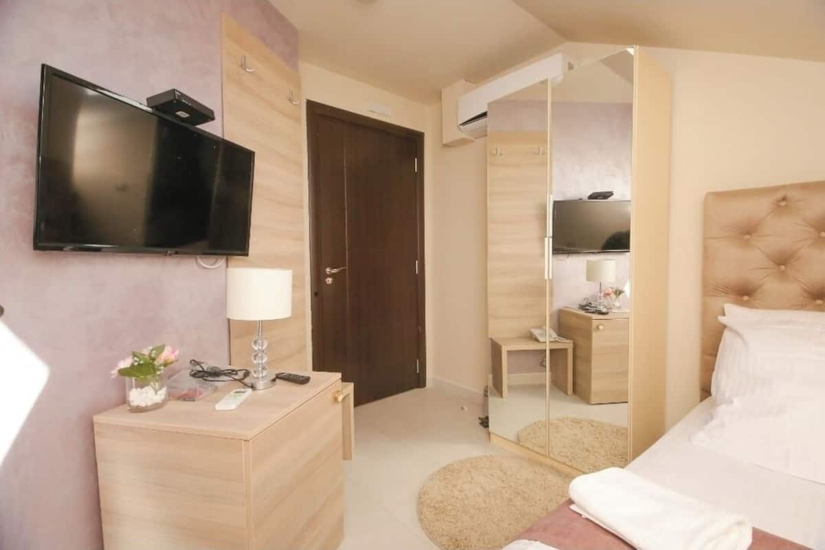 A hotel room with a bed, a TV mounted on the wall, a bedside table with a lamp, a mirror, and a wardrobe.