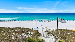 Une plage avec un poste de surveillance pour les sauveteurs, des parasols et des drapeaux.