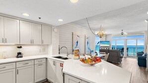 Une cuisine moderne avec des meubles blancs, un îlot central où l’on peut prendre des collations, un four encastré et une vue sur l’extérieur.