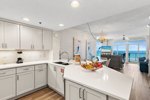 A modern kitchen with white cabinetry, a central island with snacks, a built-in oven, and a view to the outside. - Jade East 420•Beachfront•HeatedPool/Spa•Beach Gear (Destin)