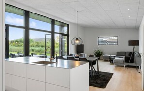 A modern kitchen with large windows, a dining area, and a living space with a sofa and lamp. - Stunning home in Hals with sauna (Hals)