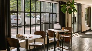 A hotel lobby with large windows, a seating area with tables and chairs, and a laptop on one of the tables. - The Industrialist Hotel Brooklyn (Brooklyn)