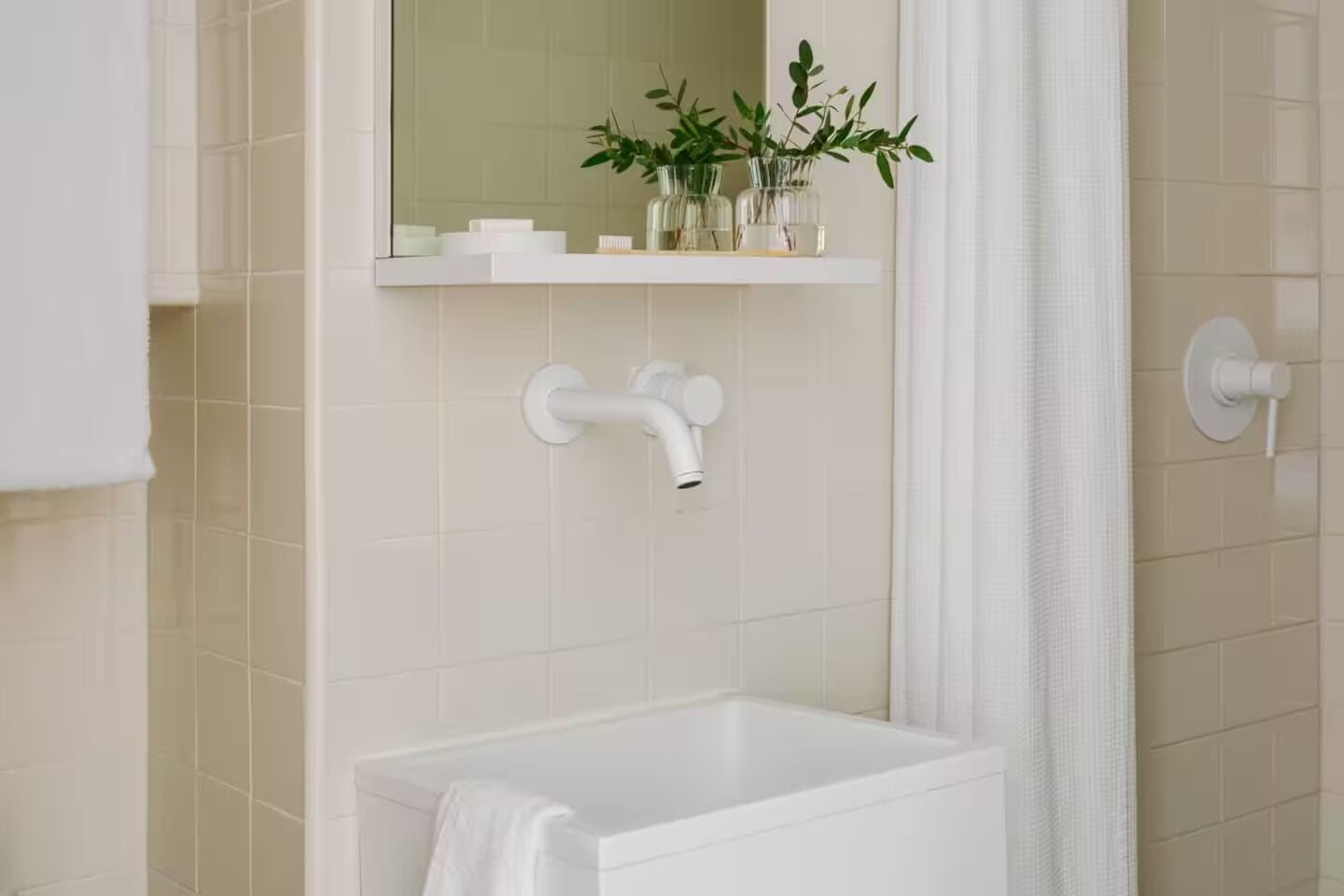 A modern bathroom with a white bathtub, a mirror above the sink, and a shelf with toiletries and plants.