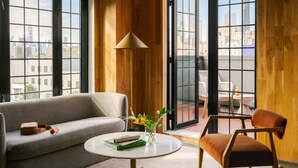 A modern living room with a grey sofa, a round coffee table, and a brown leather chair. A floor lamp and a vase with flowers are on the table. - The Industrialist Hotel Brooklyn (Brooklyn)