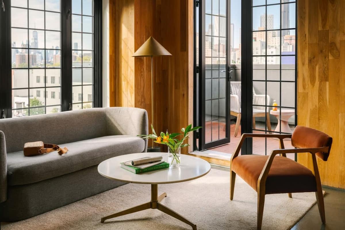 A modern living room with a grey sofa, a round coffee table, and a brown leather chair. A floor lamp and a vase with flowers are on the table.