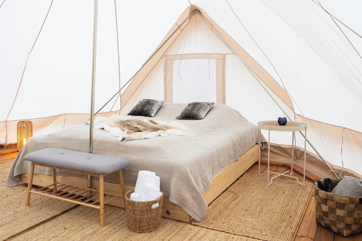 A cozy tented room with a bed, a bench, a small table, and a basket.