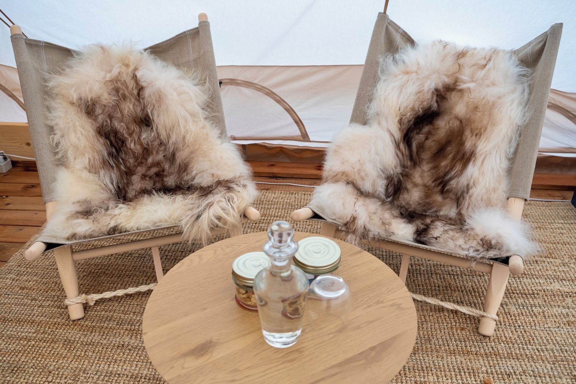 Two rustic chairs with fur upholstery, a round wooden table with salt and pepper shakers, and a woven mat on the floor.