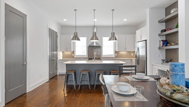 A modern kitchen with a central island, pendant lighting, and a dining area with stools. - Private Rooftop | Modern Downtown + Large Space (Nashville)