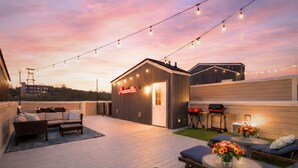 A rooftop patio with outdoor seating, string lights, and a barbecue grill. - Private Rooftop | Modern Downtown + Large Space (Nashville)