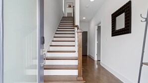 A modern interior with a wooden staircase leading to a door, white walls, and a framed mirror on the right. - Private Rooftop | Modern Downtown + Large Space (Nashville)