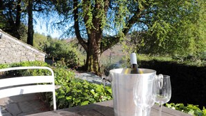 A table with a wine bottle and glasses, a stone wall, and greenery in the background. - Brockstone (Ambleside)