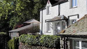 A white building with a stone wall, a window, and a door. - Brockstone (Ambleside)