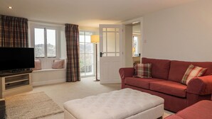 A living room with a television, red sofa, and a large window with curtains. - Brockstone (Ambleside)