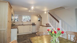 A kitchen with a wooden table and chairs, a vase with flowers, and a staircase. - Brockstone (Ambleside)