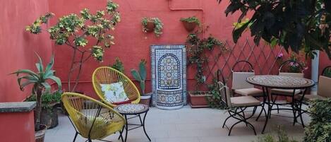 A courtyard with yellow wicker chairs, a round table, and potted plants.