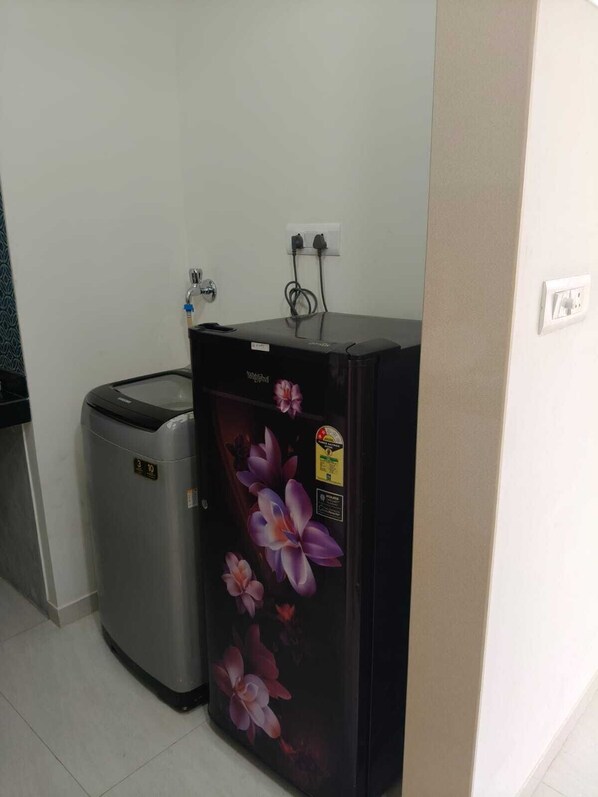 Une petite cuisine équipée d’un réfrigérateur, d’une poubelle et d’une prise électrique au mur.