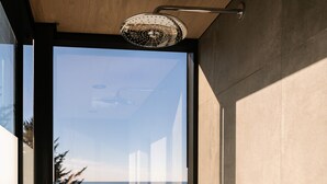 A modern bathroom with a glass door leading to a balcony, a showerhead, and a wall-mounted faucet. - South Cape Mirror Cabin, Queen - Floor to Ceiling Expansive Views (Cloverdale)