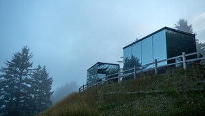 A modern glass building with a wooden fence on a grassy hill. - South Cape Mirror Cabin, Queen - Floor to Ceiling Expansive Views (Cloverdale)