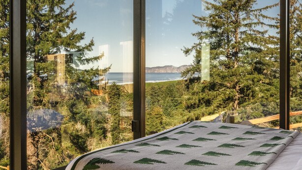 A bedroom with a large window offering a view of trees and a body of water. - South Cape Mirror Cabin, Queen - Floor to Ceiling Expansive Views (Cloverdale)