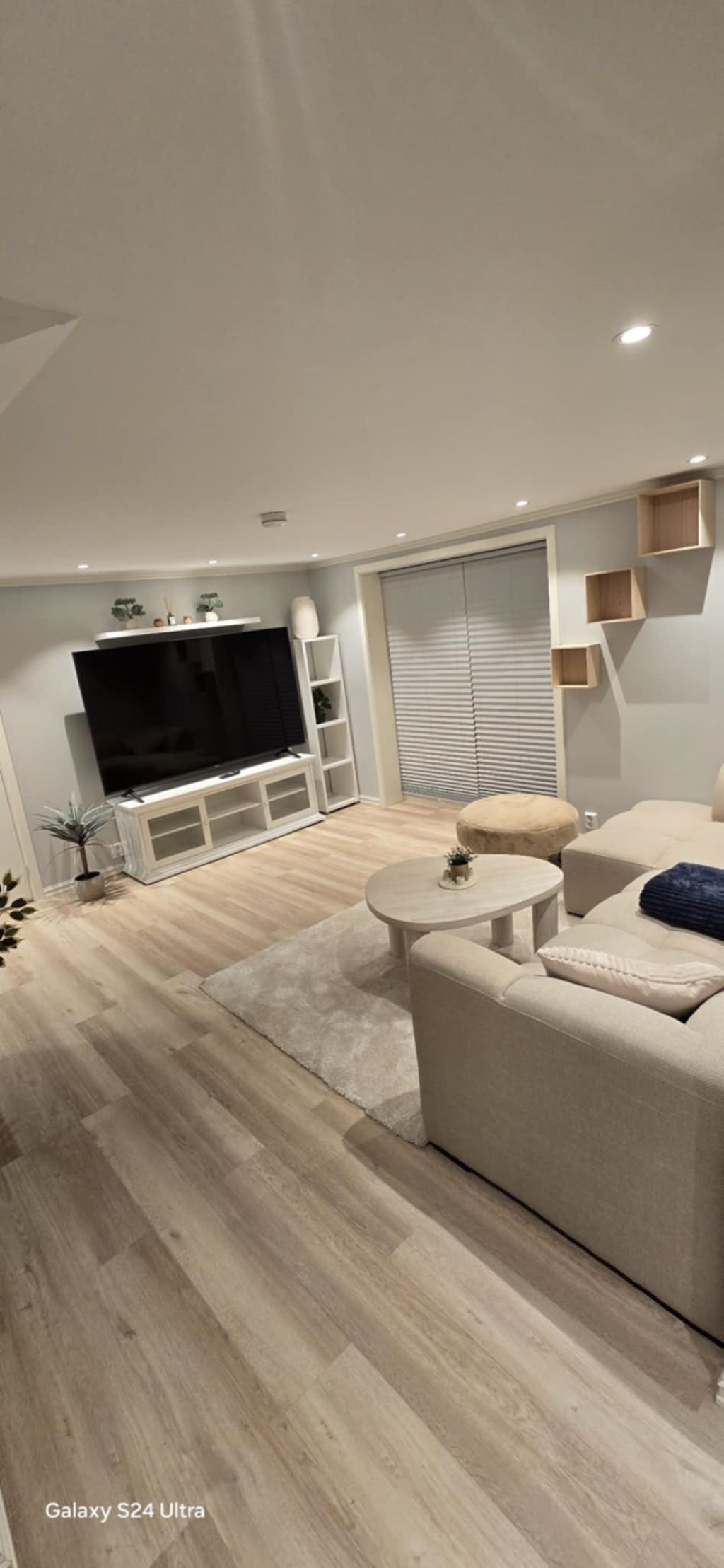 Una sala de estar moderna con un televisor de pantalla plana, un sofá, una mesa redonda de centro y piso de madera.