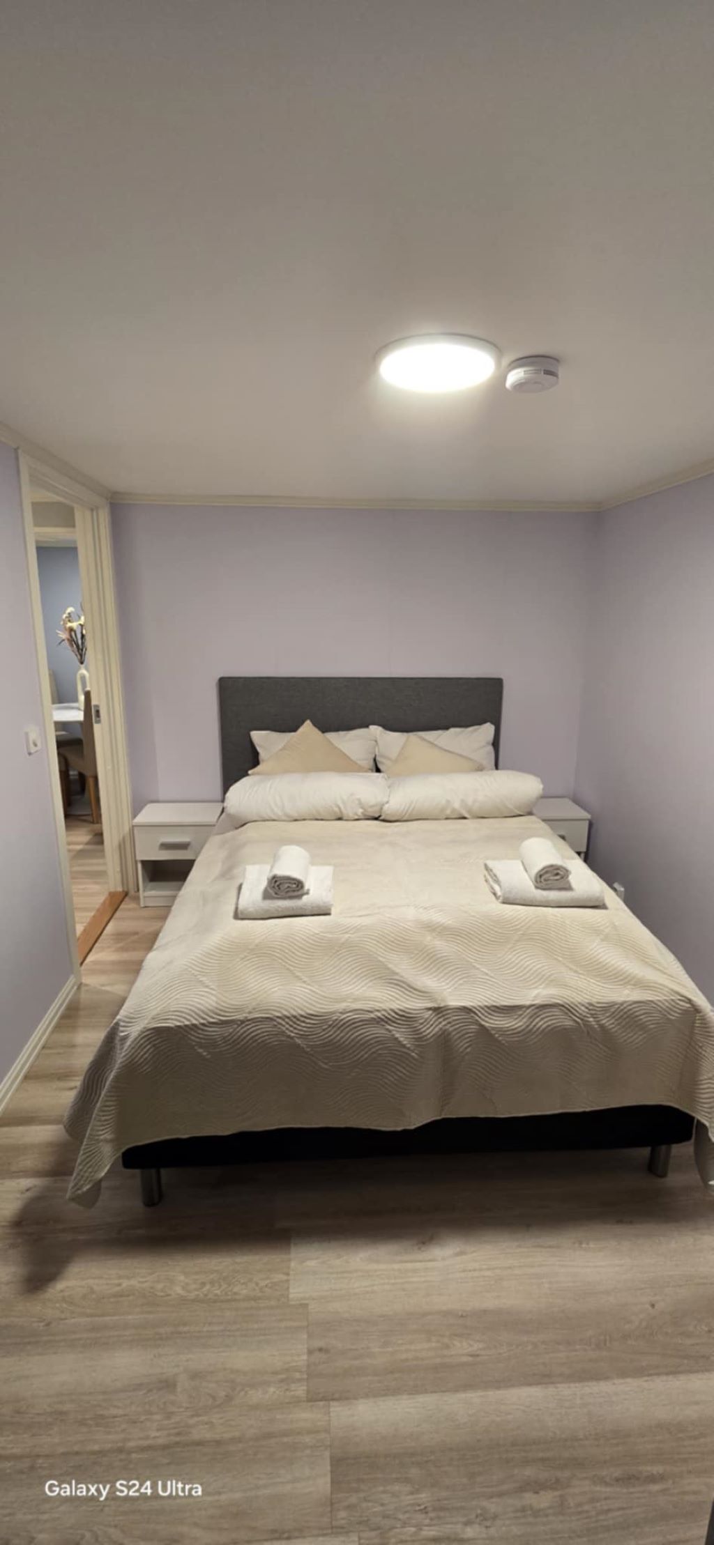 Una cama bien hecha con cabecera, mesita de noche y tocador.