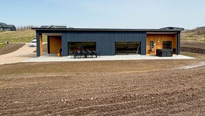 Ein modernes Gebäude mit einer großen, offenen Terrasse, einem überdachten Sitzbereich im Freien und einem in der Nähe geparkten Auto.