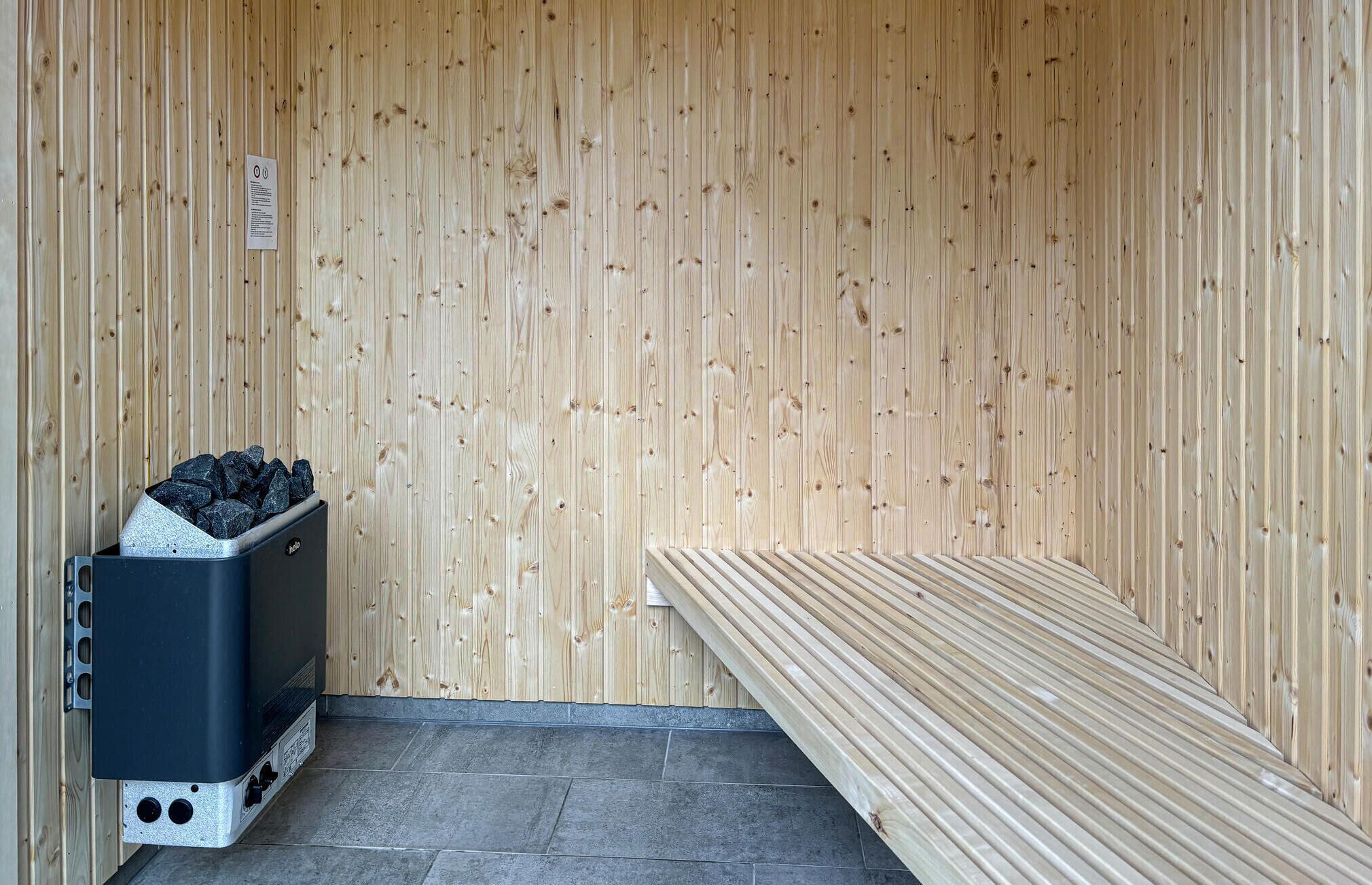 A sauna room with a bench, a heater, and a container of charcoal.