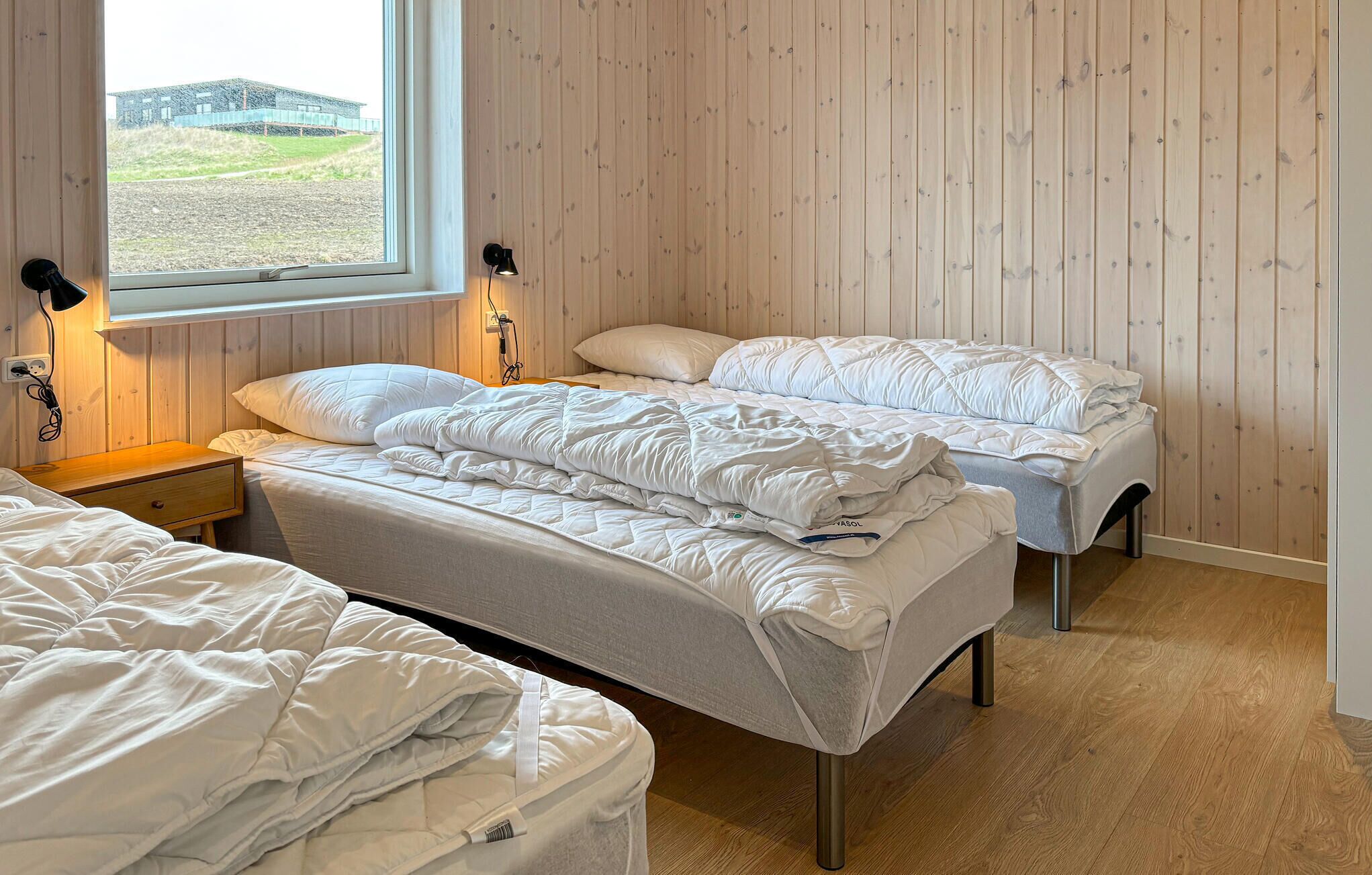 Et soveværelse med to senge, et vindue med udsigt, trævægge og et natbord med lampe.