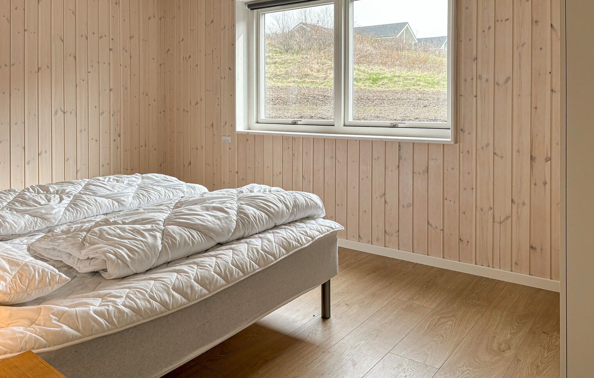 Une chambre à coucher avec un lit, des murs en bois, une fenêtre et une vue sur l’extérieur.