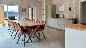 Eine moderne Küche mit Holzausstattung, ein Essbereich mit großem Tisch und Stühlen sowie Blick durch die Glastür.