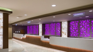 Zona de recepción de hotel con mostrador de registro y un muro con un diseño luminoso morado.