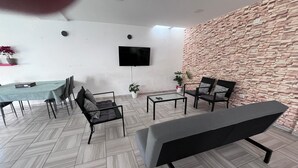 Un salon moderne avec un mur en pierre, un téléviseur à écran plat et un espace détente comprenant un banc et des fauteuils.