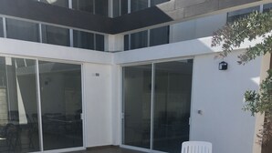 Un espace piscine extérieur moderne, doté d’un jacuzzi, d’une chaise blanche et d’une porte vitrée donnant accès à un espace intérieur.