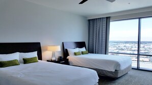 Een hotelkamer met twee bedden, een nachtkastje met een lamp en een groot raam met uitzicht op de stad.