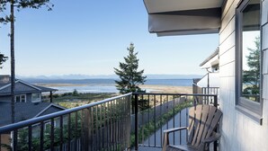 A balcony with a view of the beach and mountains, a wooden chair, and a railing.