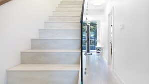 A modern staircase with a glass railing, leading to a bright hallway with a door at the end.