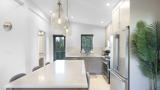 A modern kitchen with a large island, stainless steel appliances, and a hanging light fixture.