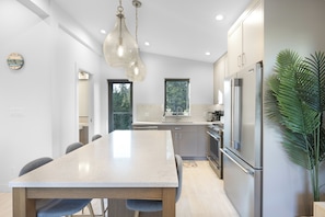 A modern kitchen with a large island, stainless steel appliances, and a hanging light fixture.