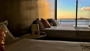 Ein Zimmer mit zwei Betten, einem kleinen Tisch und Blick auf das Meer bei Sonnenuntergang.