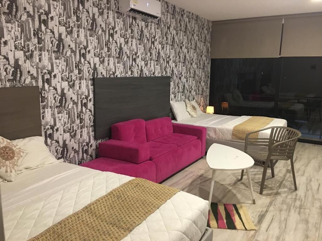Ein Hotelzimmer mit zwei Betten, einem rosa Sofa, einem kleinen weißen Tisch und Blick auf die Stadt durch ein großes Fenster.