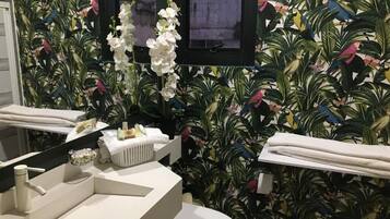 A bathroom with a modern sink, toilet, and a mirror. There is a decorative plant and a framed picture on the wall.