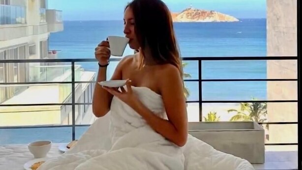 Eine Person sitzt auf einem Balkon mit Blick auf das Meer und eine entfernte Insel.