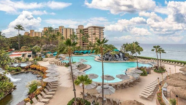 Resort com piscina grande, palmeiras e vista para o mar.