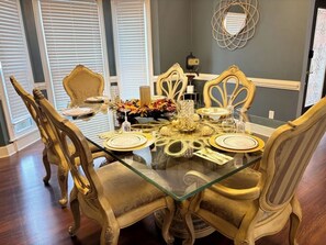 Una mesa de comedor con sillas decorativas, un tablero de vidrio y un centro de mesa floral.
