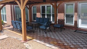 Ein überdachter Patio-Bereich mit Gartenmöbeln und einem Backsteingebäude im Hintergrund.