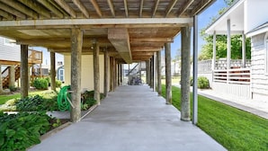 Ein überdachter Außenweg mit Holzbalken und Säulen, der zu einem Gebäude mit weißer Fassade führt.